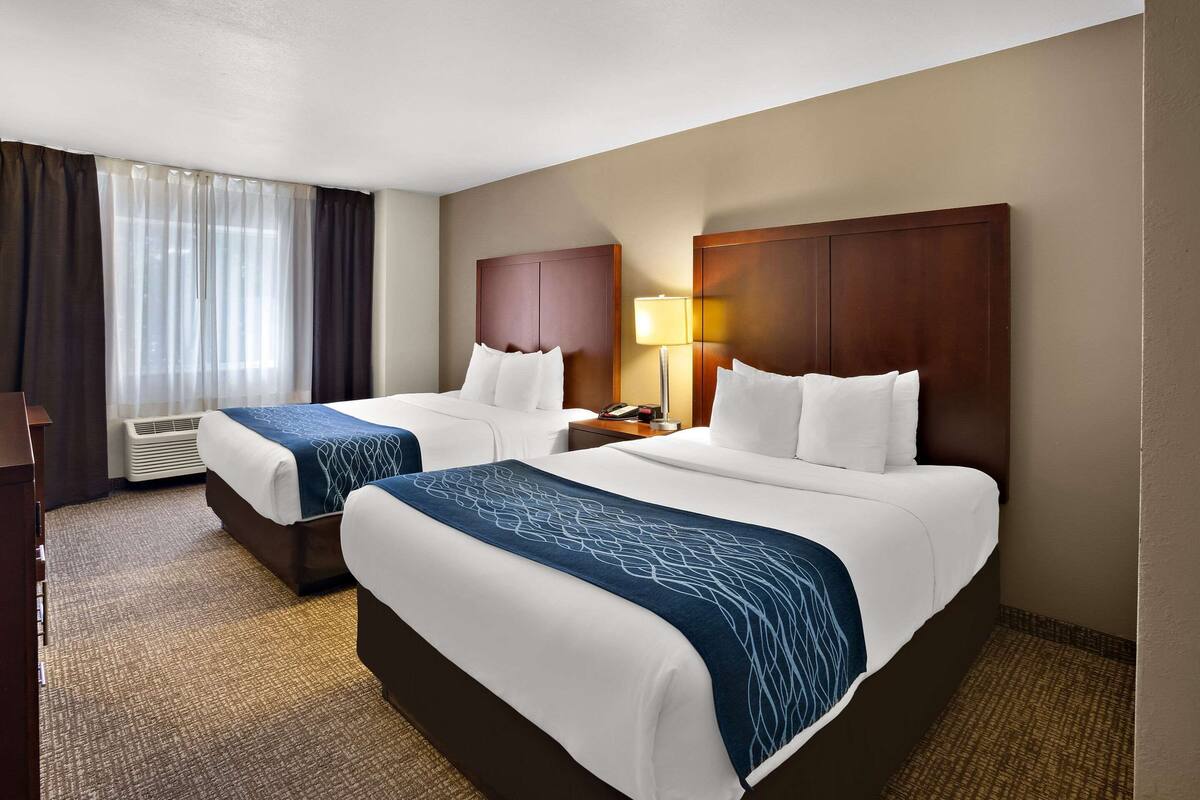A hotel room with two beds, a desk, a lamp, and a window with curtains.