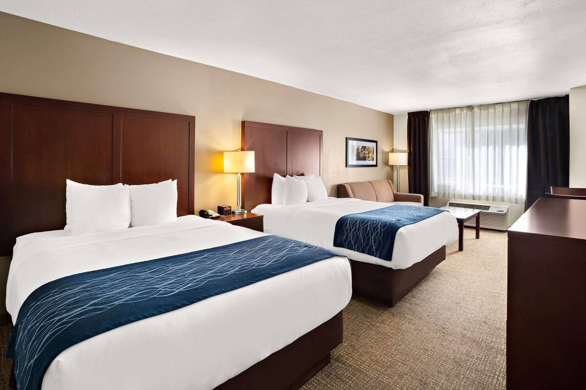 A hotel room with two beds, a desk, a chair, a lamp, and a window with curtains.