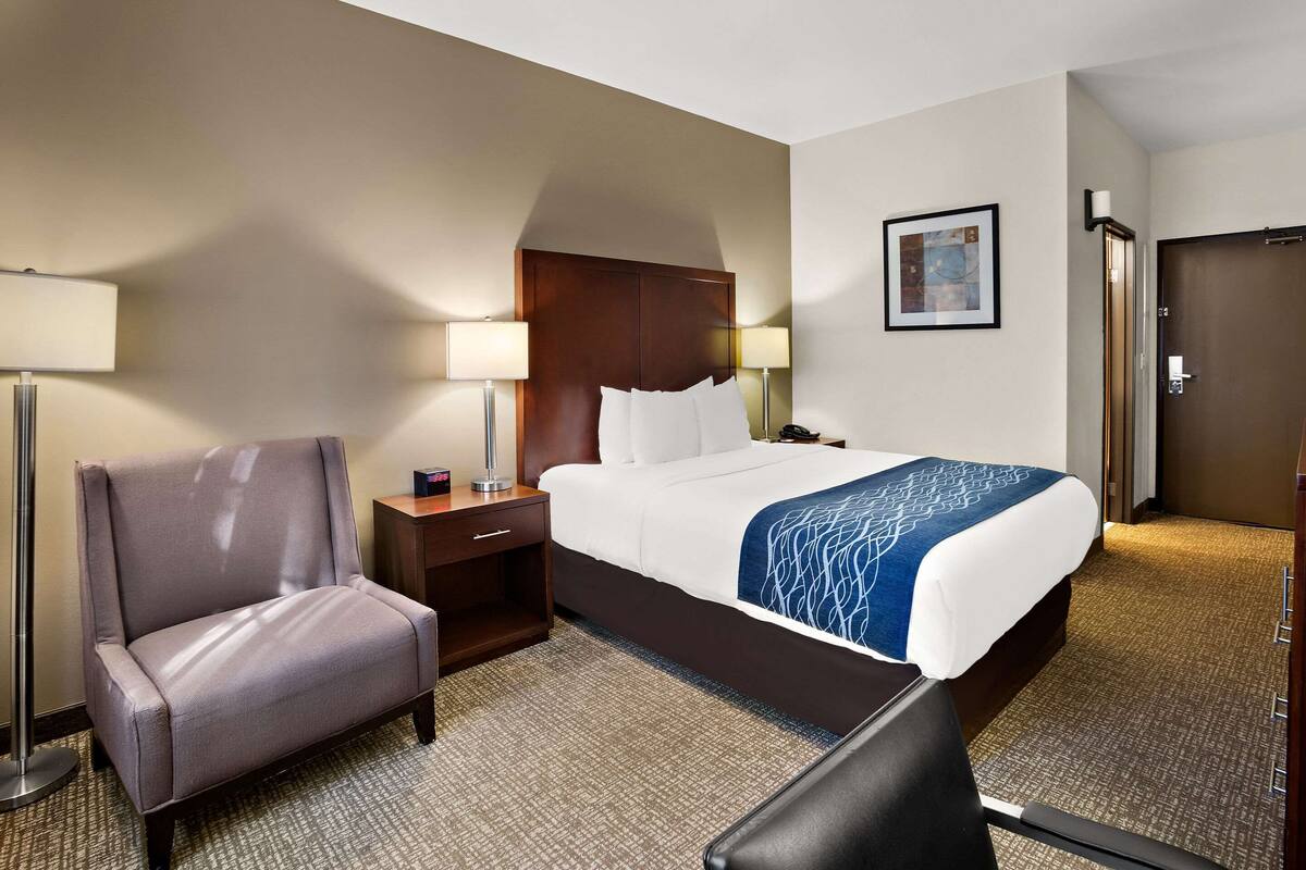 A hotel room with a large bed, a chair, a desk, and a lamp.