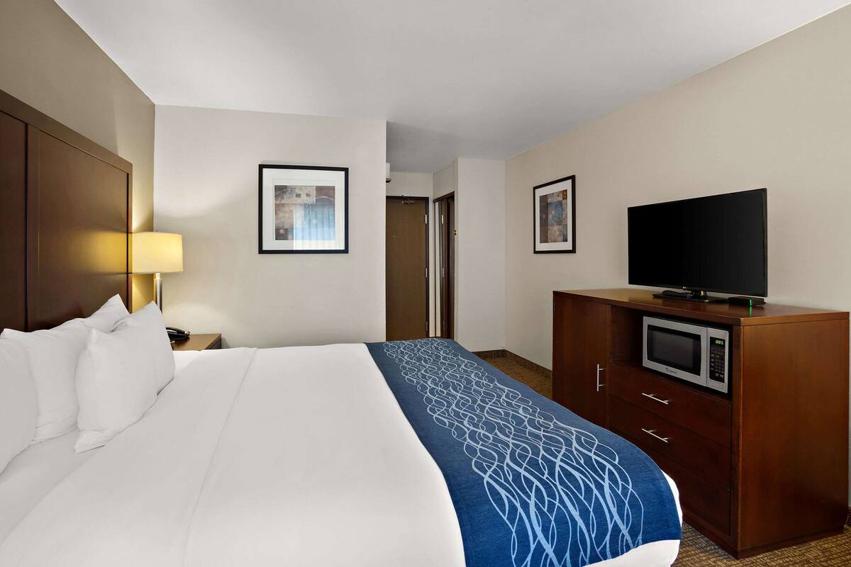 A hotel room with a large bed, a TV on a wooden cabinet, and framed pictures on the walls.