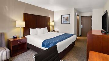 A hotel room with a large bed, a desk, a chair, a TV, and a lamp.
