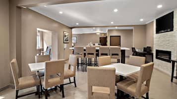 A dining area with multiple tables and chairs, a clock, and a flat-screen TV mounted on the wall.