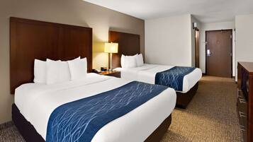 A hotel room with two beds, a nightstand with a lamp, a wooden headboard, and a carpeted floor.