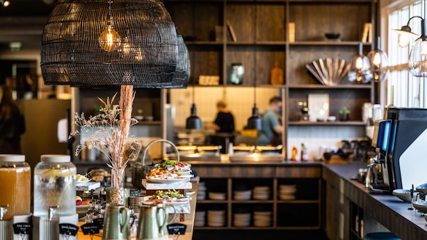 A restaurant interior with a buffet setup, bar stools, and a hanging light fixture.