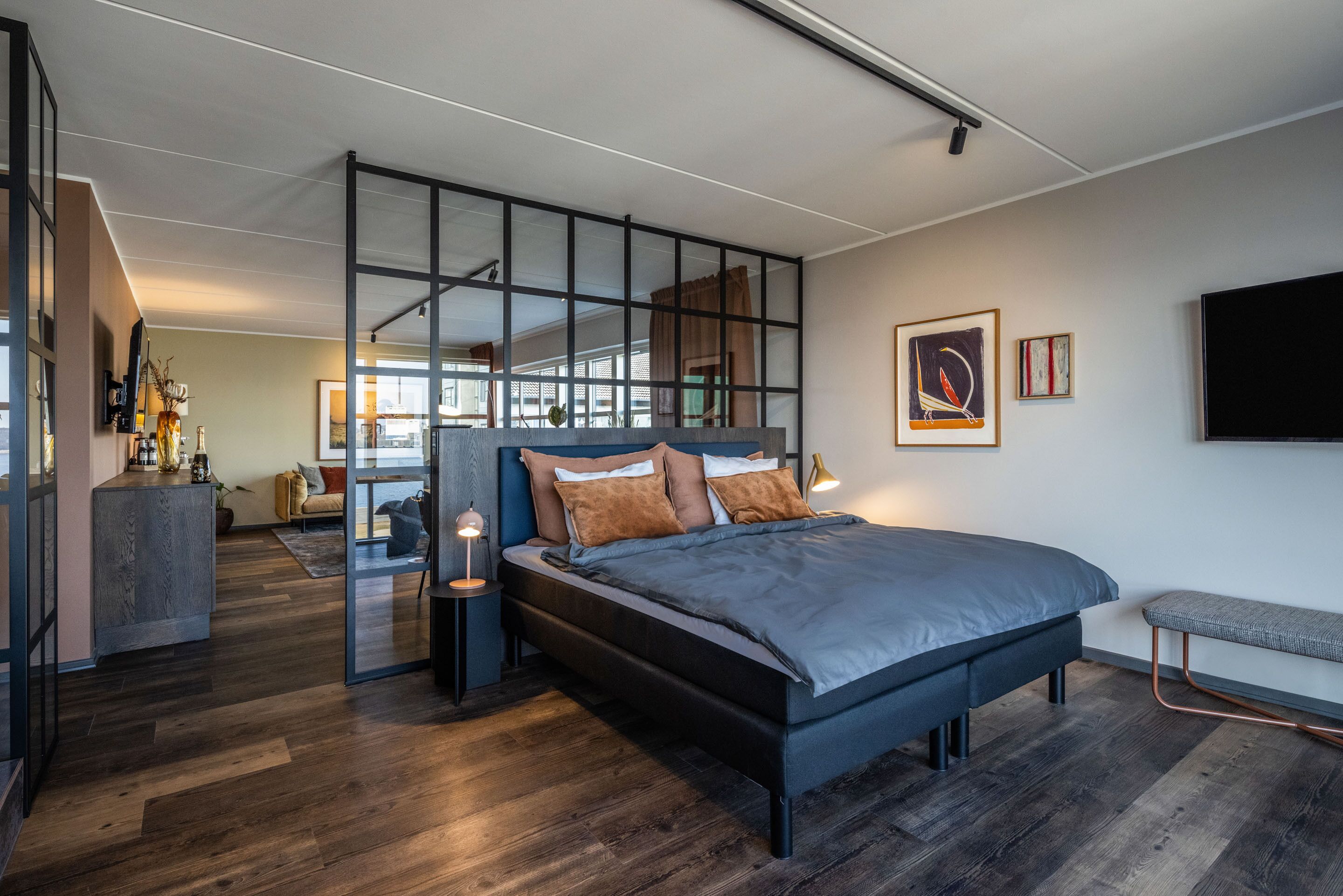 A modern bedroom with a large bed, a desk, and a glass partition.