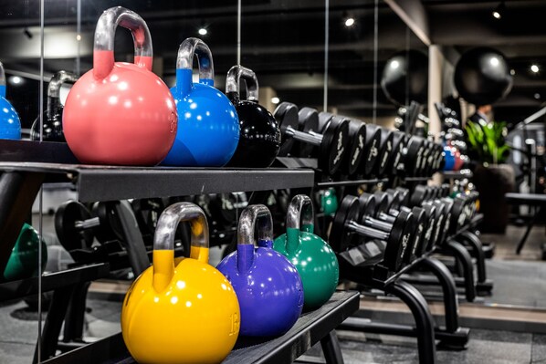 Kettlebells in various colors arranged on a rack in a gym setting.