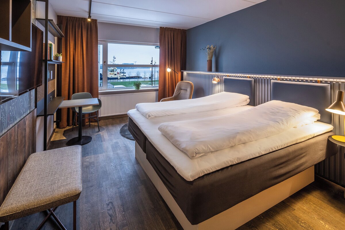 A hotel room with a large bed, a desk, a chair, and a view of the outside.