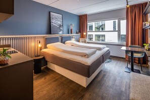 A modern hotel room with a large bed, a desk, and a view of the city.