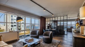 A modern living room with a large window, a sofa, a coffee table, and a dining area with chairs and a table.