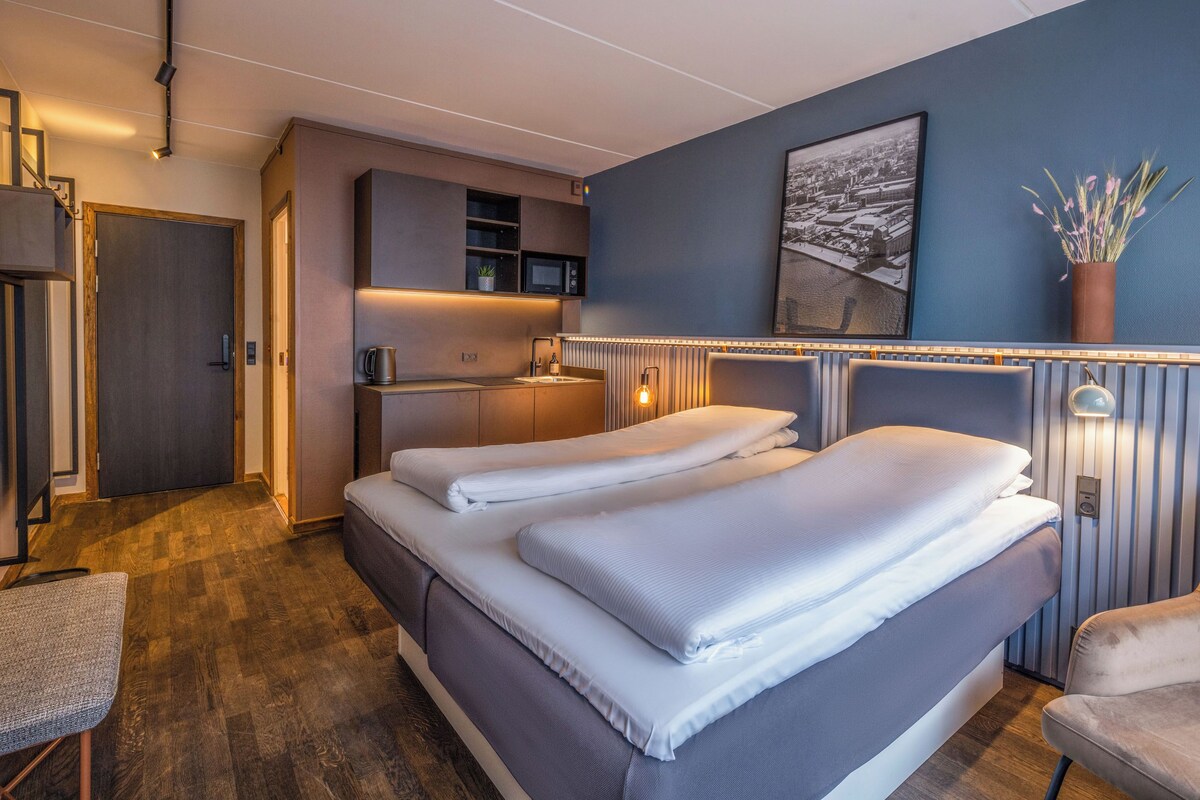 A modern hotel room with a large bed, a desk, and a view of the city.