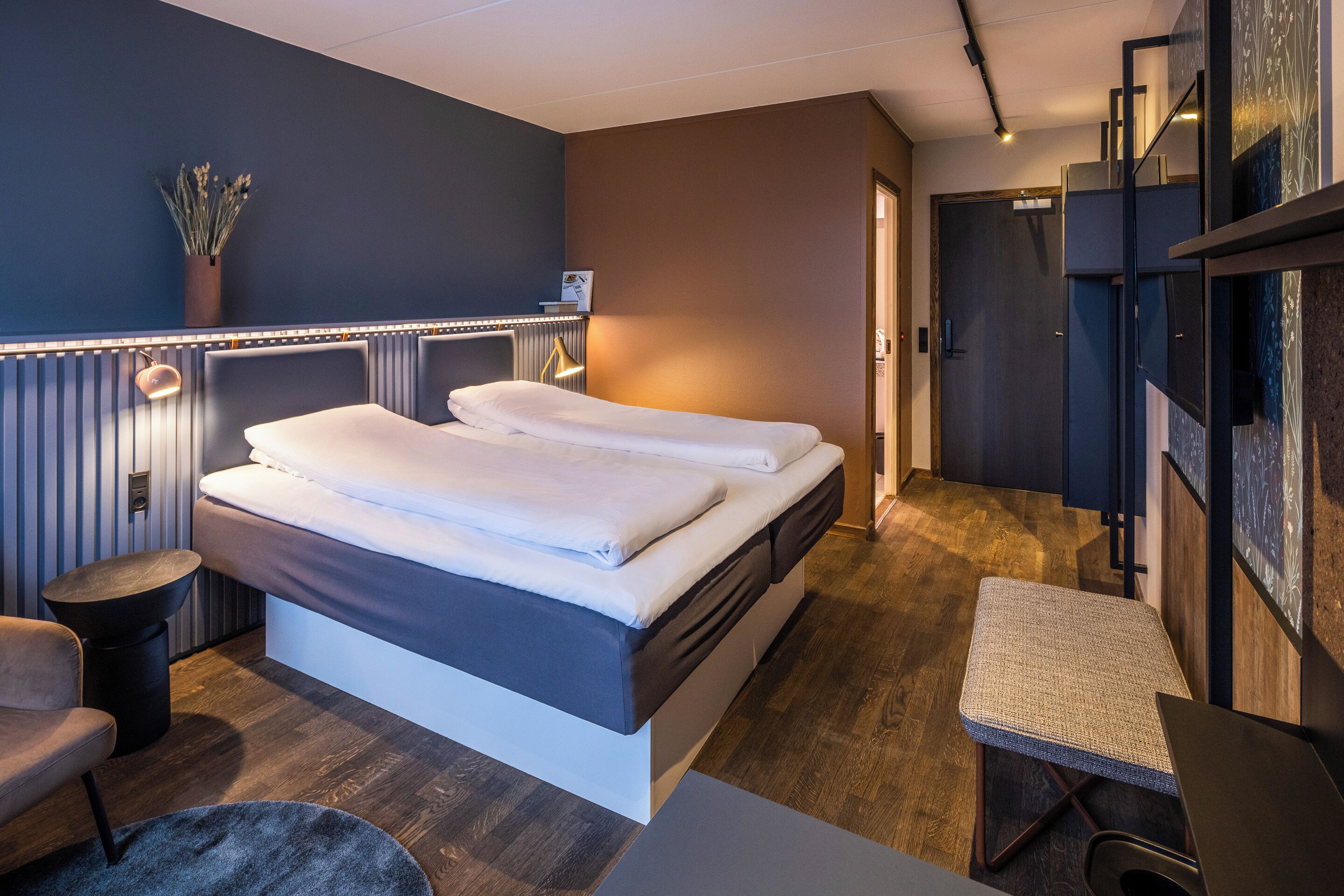 A modern hotel room with a bed, a small seating area, and a desk.