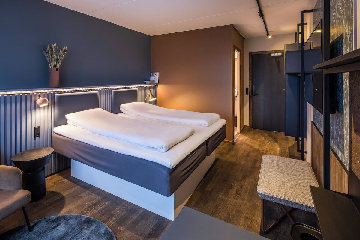 A modern hotel room with a bed, a small seating area, and a desk.