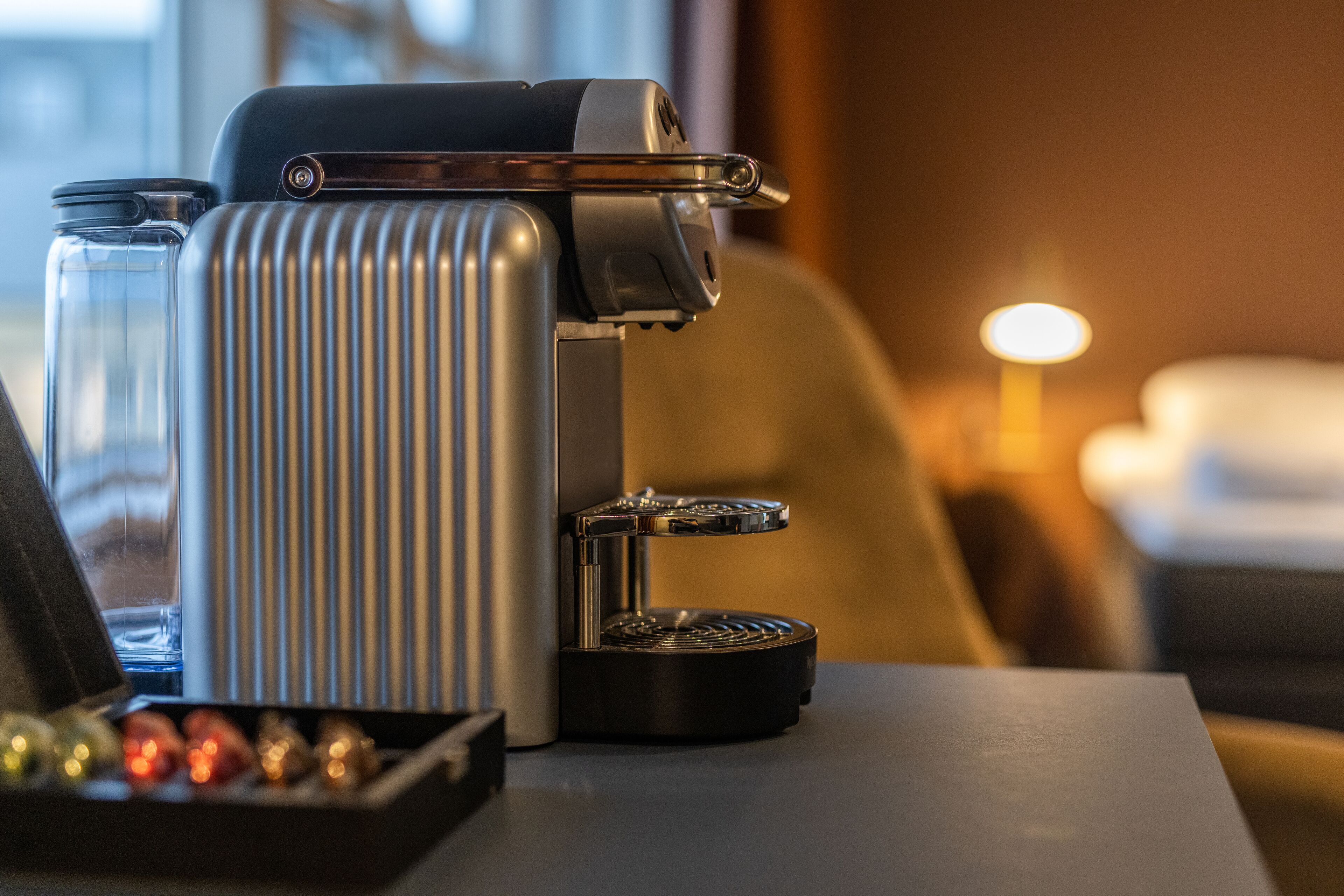A coffee machine on a table with a glass container and a box of chocolates.