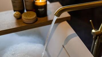 A bathroom with a running faucet, a candle, and a bottle on a shelf.