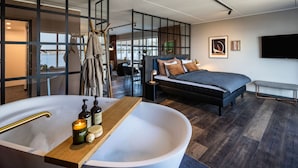 A modern bedroom with a large bathtub, a bed, and a desk area.