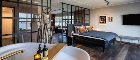 Un dormitorio moderno con una bañera grande, una cama y una zona de escritorio.