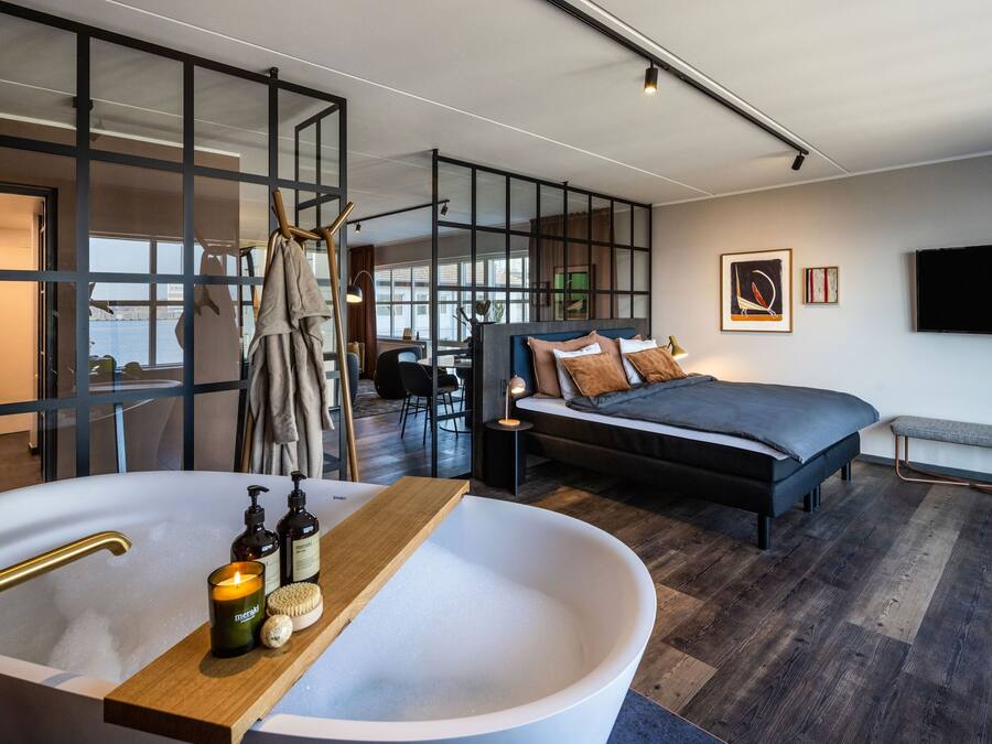 A modern bedroom with a large bathtub, a bed, and a desk area.