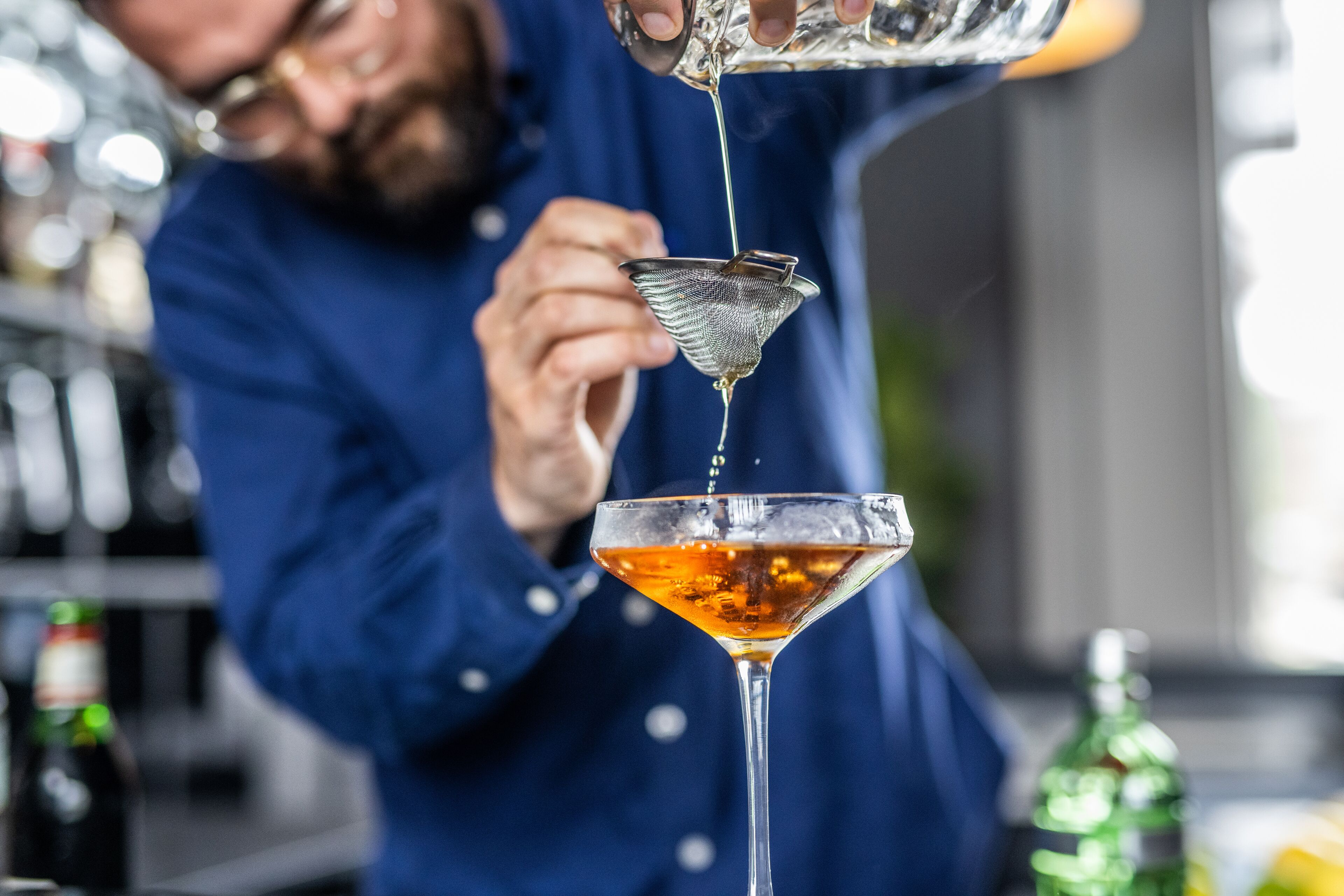 A bartender pouring a drink into a martini glass.