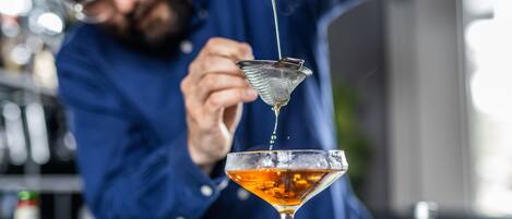 Ein Barkeeper gießt ein Getränk in ein Martini-Glas ein.