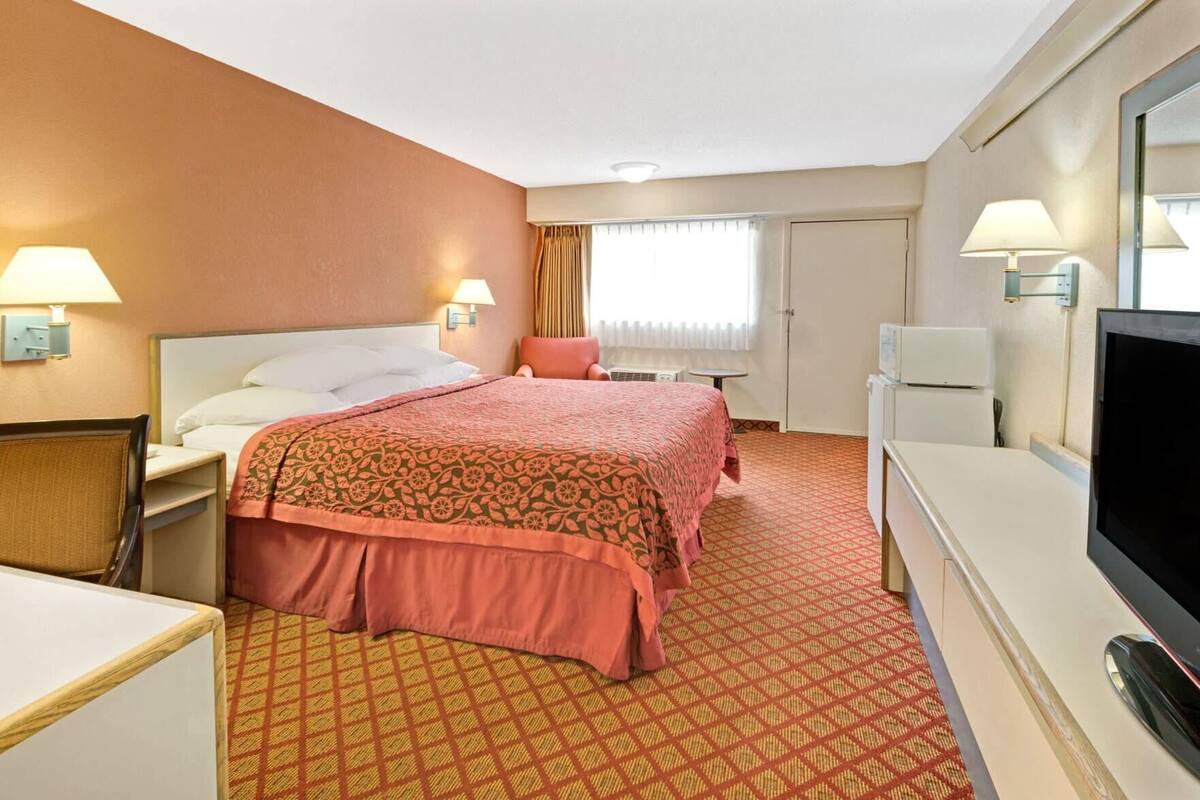 Een hotelkamer met een bed, twee nachtkastjes, een bureau, een televisie en een raam met gordijnen.