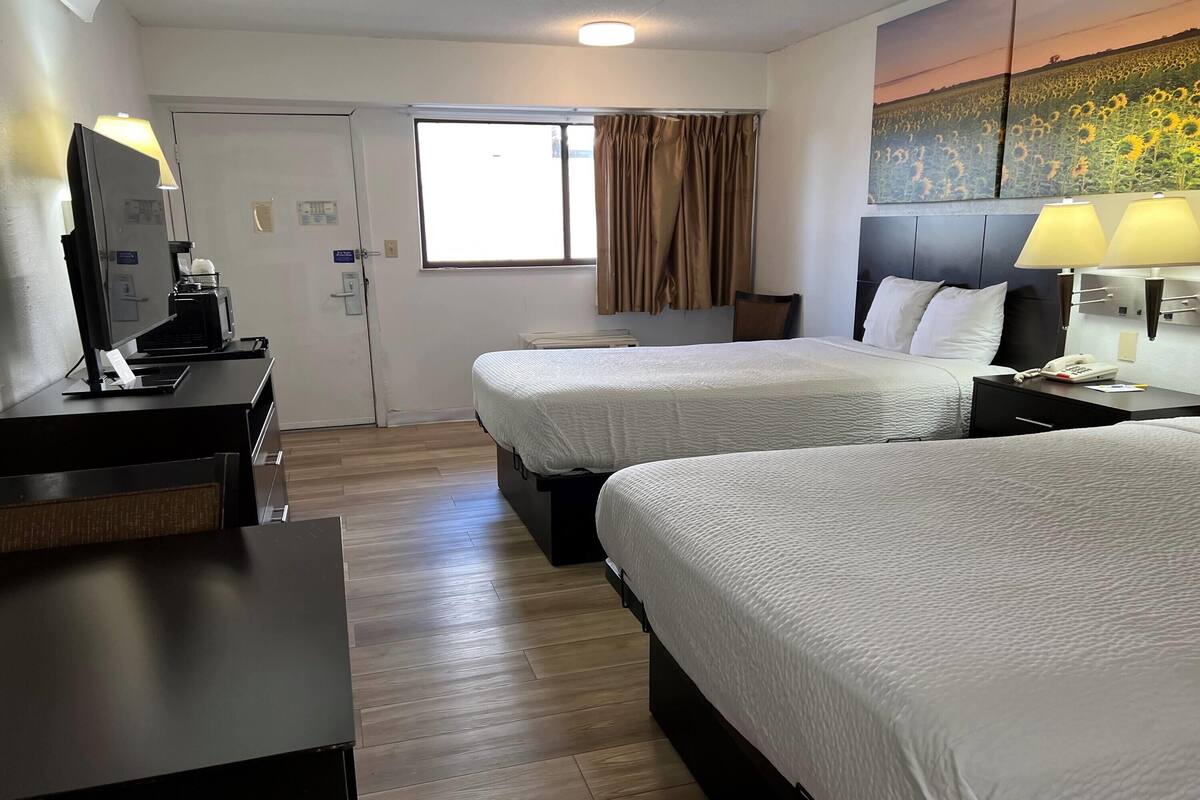 Een hotelkamer met twee bedden, een bureau met een koffiezetapparaat, een raam met gordijnen en een schilderij aan de muur.
