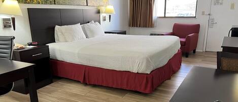 A hotel room with a large bed, a desk, a chair, and a window with curtains.