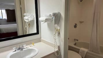 A hotel bathroom with a white sink, a mirror, a hairdryer, and a shower.
