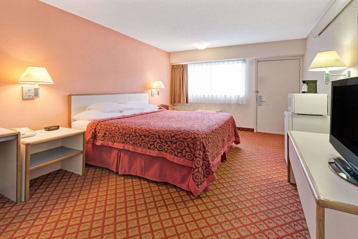Een hotelkamer met een bed, nachtkastjes, een televisie en een raam met gordijnen.