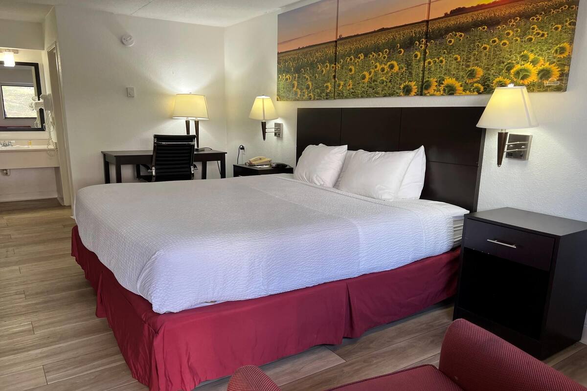 Een hotelkamer met een groot bed, twee nachtkastjes met lampen, een bijzettafeltje en een rode stoel.
