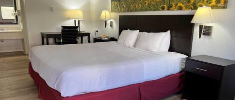A hotel room with a large bed, two bedside tables with lamps, a nightstand, and a red chair.