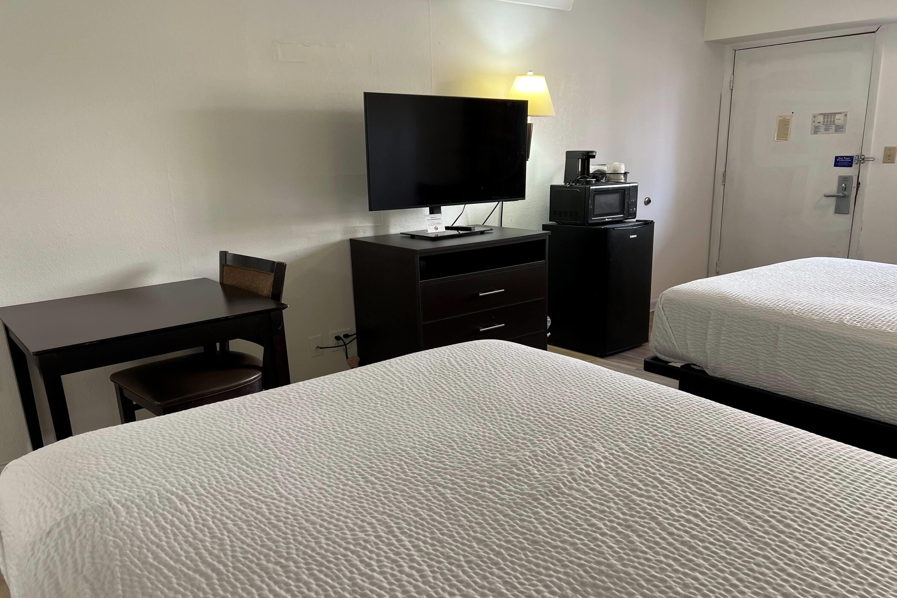 A hotel room with two beds, a desk, a television, a coffee maker, and a microwave.