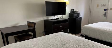 A hotel room with two beds, a desk, a television, a coffee maker, and a microwave.