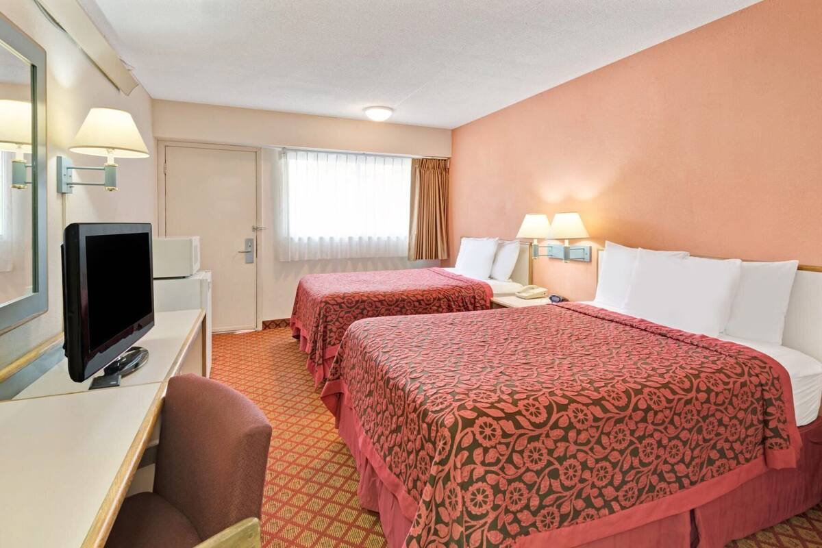 Een hotelkamer met twee bedden, een bureau met een televisie en een raam met gordijnen.