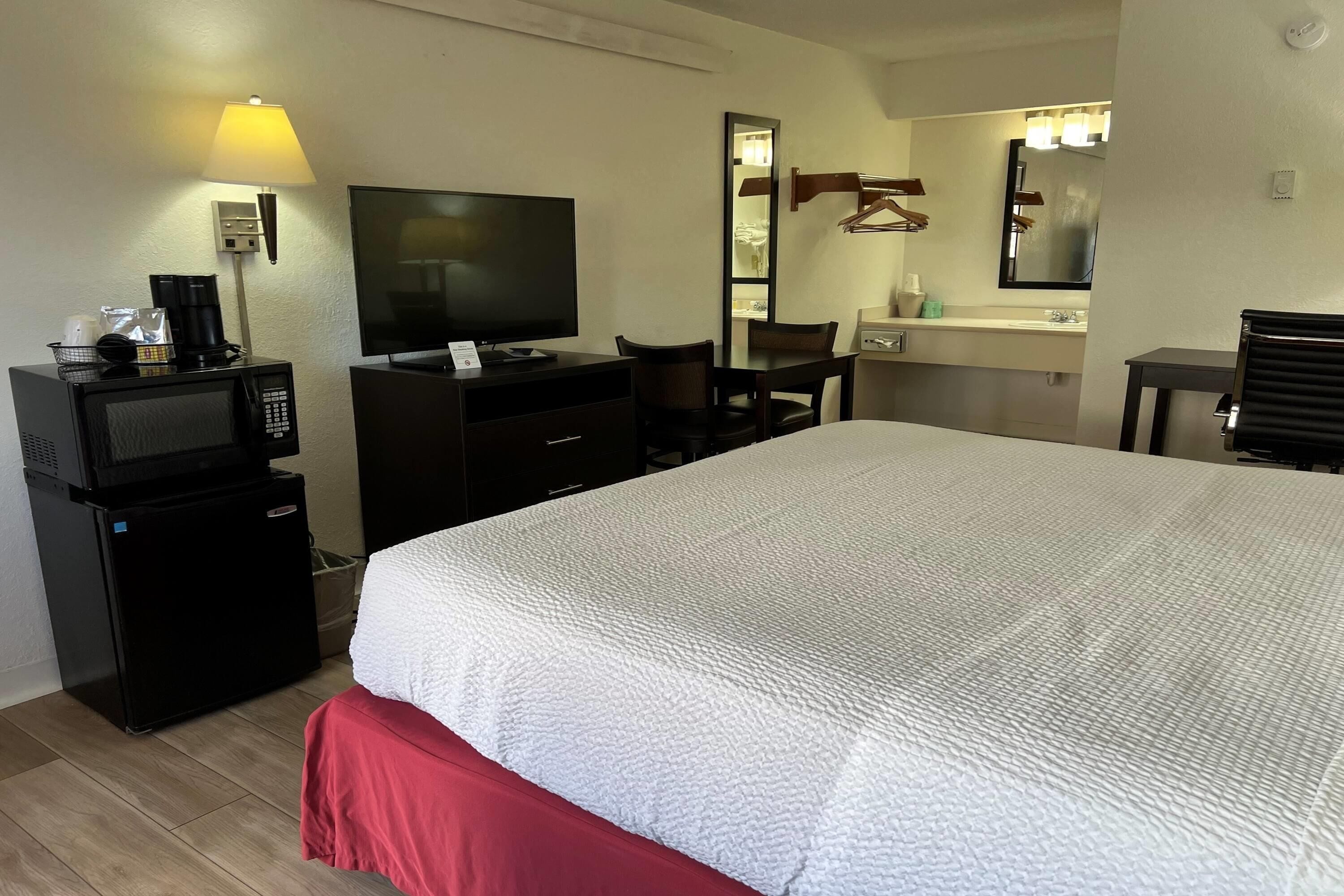Ein Hotelzimmer mit einem Bett, einem Schreibtisch mit Computer, einem Fernseher, einer Mikrowelle, einer Kaffeemaschine und einem Spiegel.