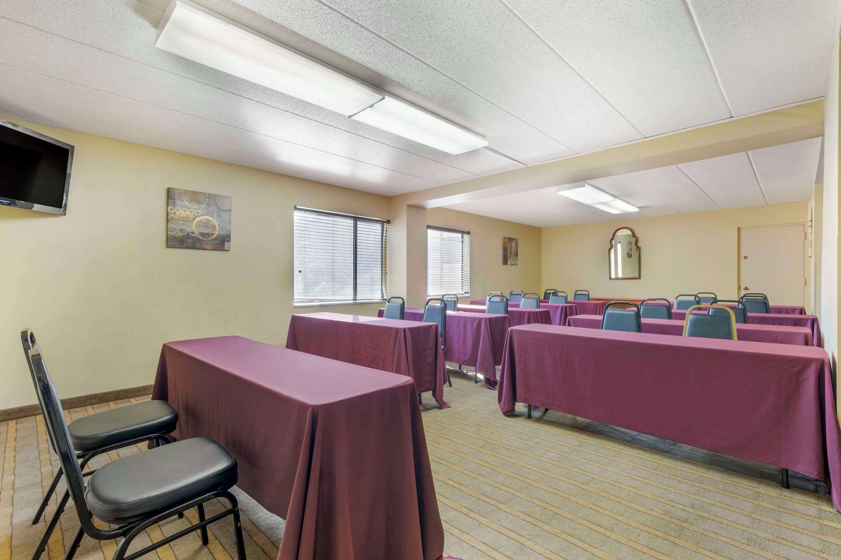 A conference room with tables covered in purple tablecloths, a television mounted on the wall, and a window with blinds.