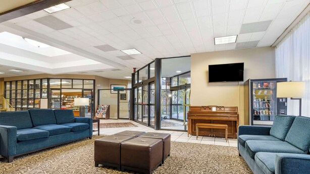A hotel lobby with a blue sofa, a piano, a television, and a vending machine.