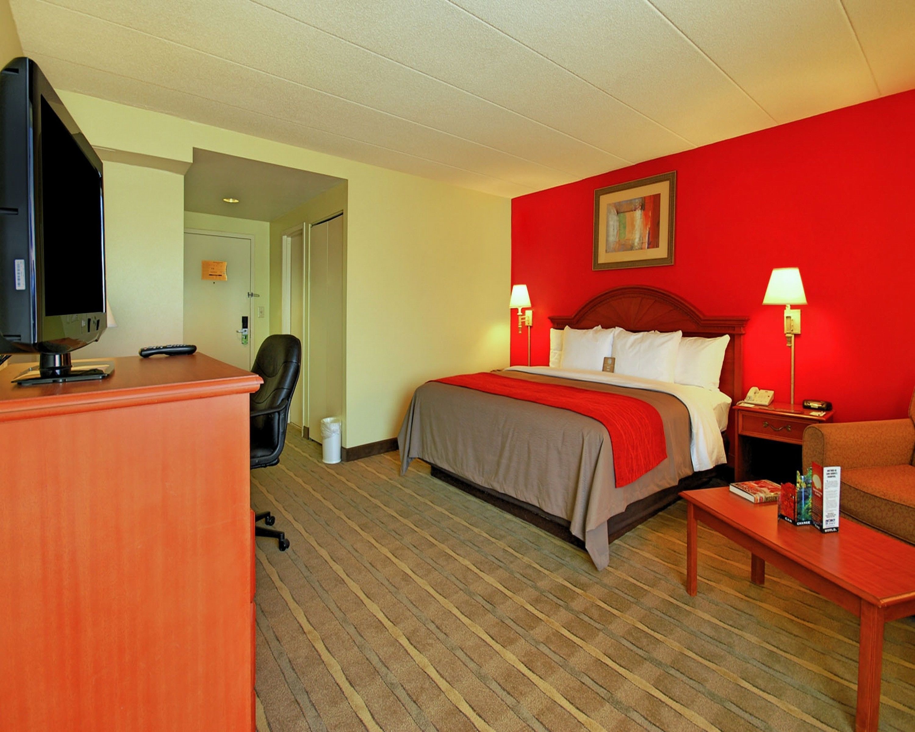 Ein Hotelzimmer mit einem Bett, einem Schreibtisch, einem Stuhl, einem Fernseher und einer Lampe.