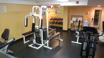Un gimnasio con equipo de ejercicio variado, incluyendo una banca, máquinas de pesas y una cinta de correr.