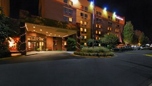 A hotel with a well-lit entrance, a covered waiting area, and a landscaped garden.