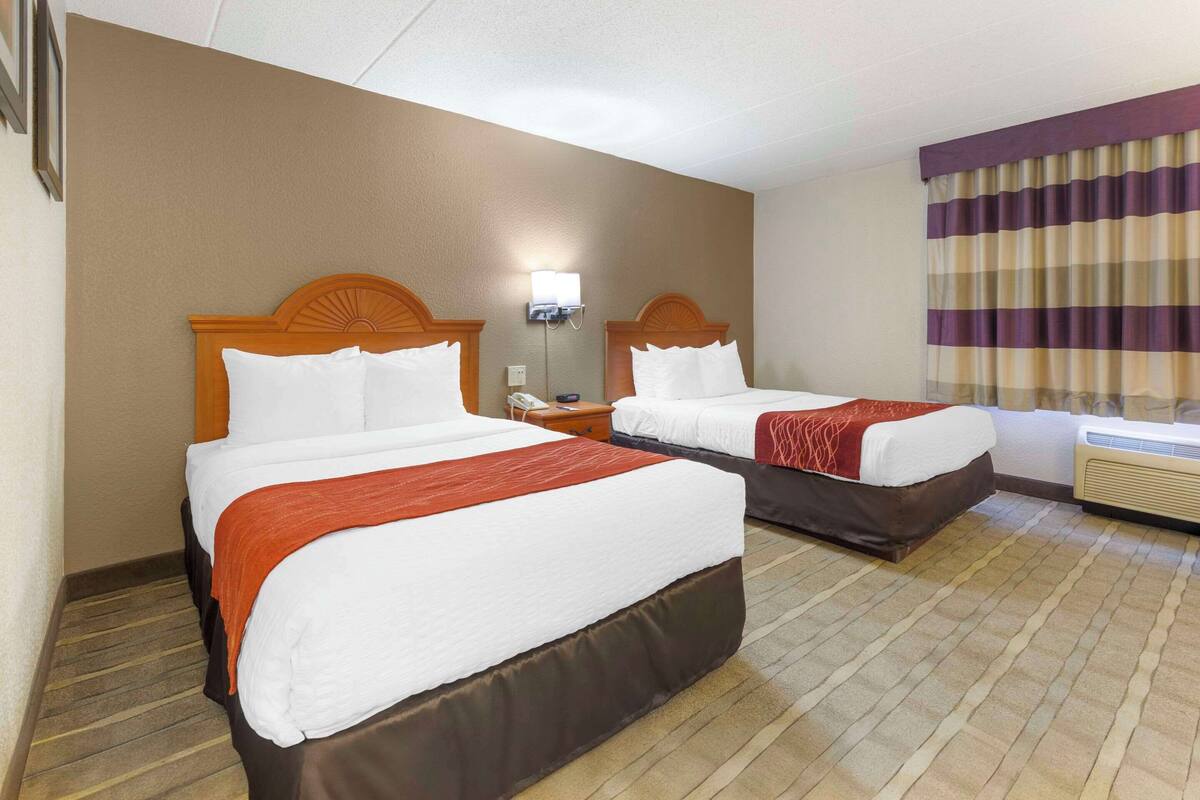 A hotel room with two beds, a nightstand, a lamp, and a window with curtains.
