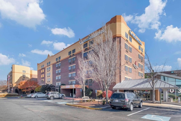 A hotel with multiple floors, a parking lot, and a small outdoor seating area.