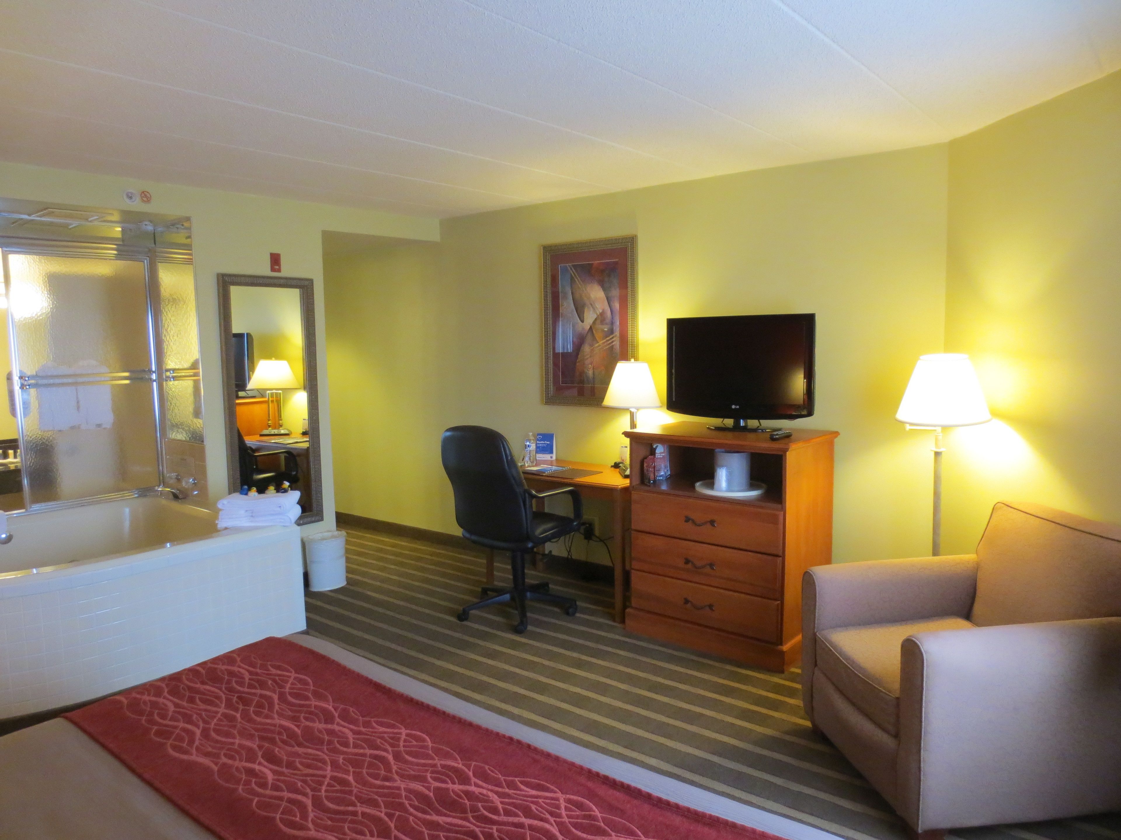 A hotel room with a bathtub, desk, chair, television, and two lamps.
