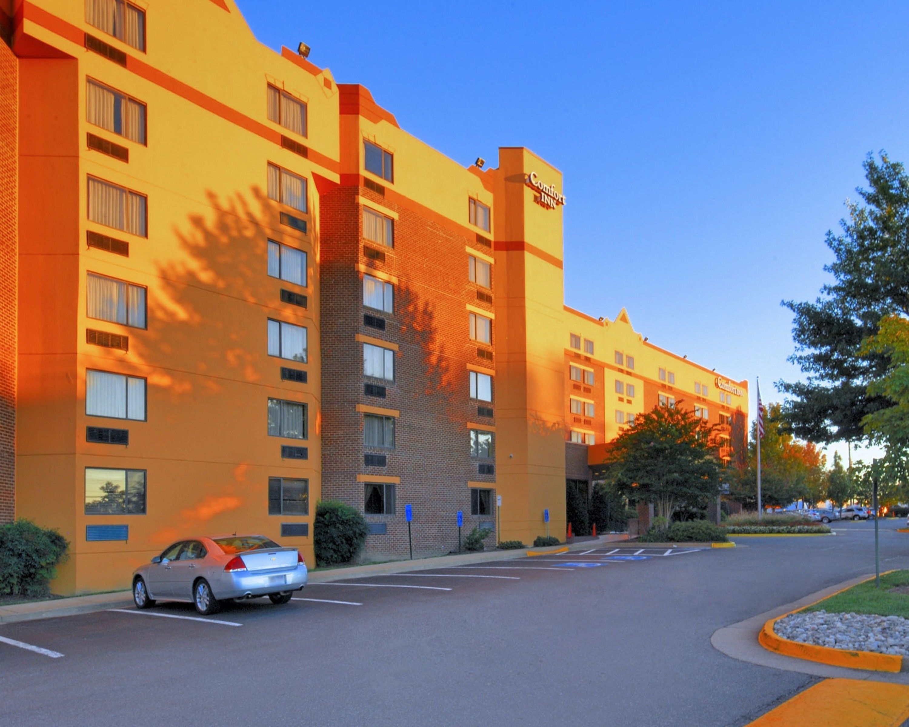 A multi-story hotel with a brick facade and a flat roof, featuring a parking lot with a single car.