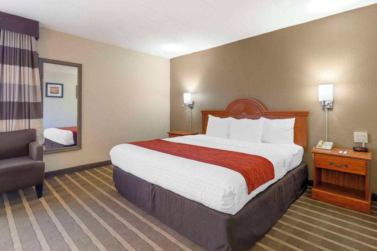 A hotel room with a large bed, a chair, a nightstand, and a mirror.