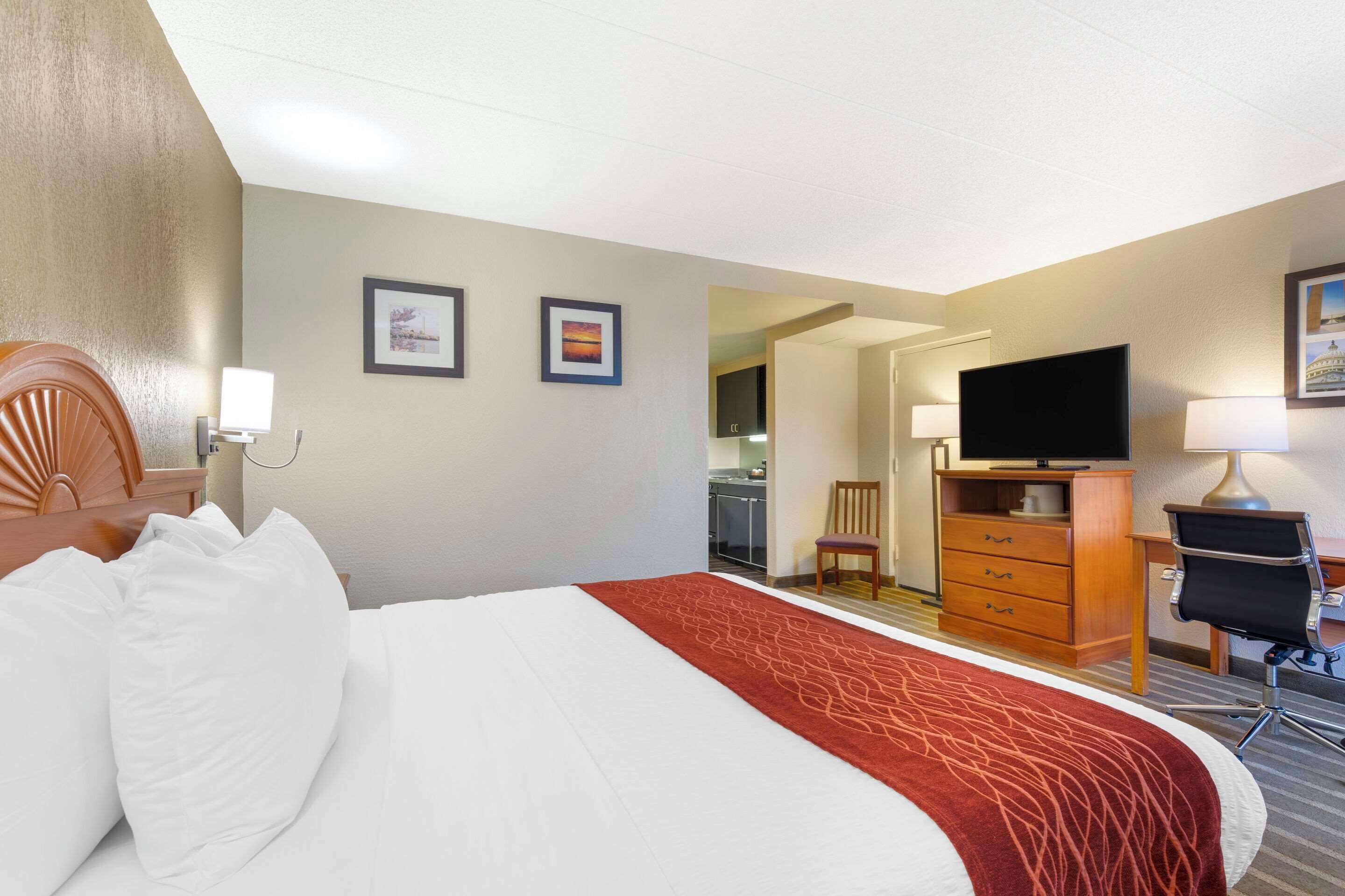 Habitación de hotel con cama, escritorio, silla, televisor y baño visible a través de una puerta abierta.