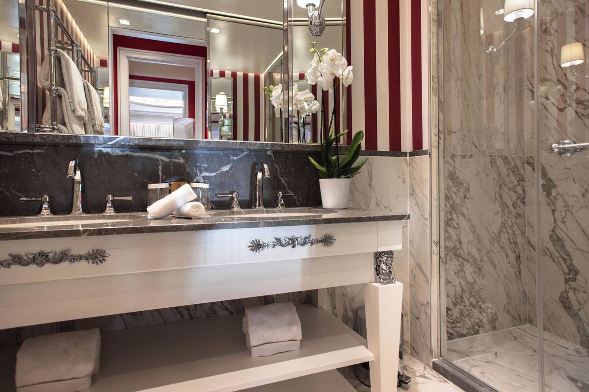 A bathroom with a marble vanity, a large mirror, a potted orchid, and a shower area.