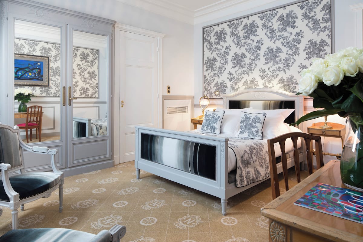 A bedroom with a bed, a chair, a table, and a mirror.