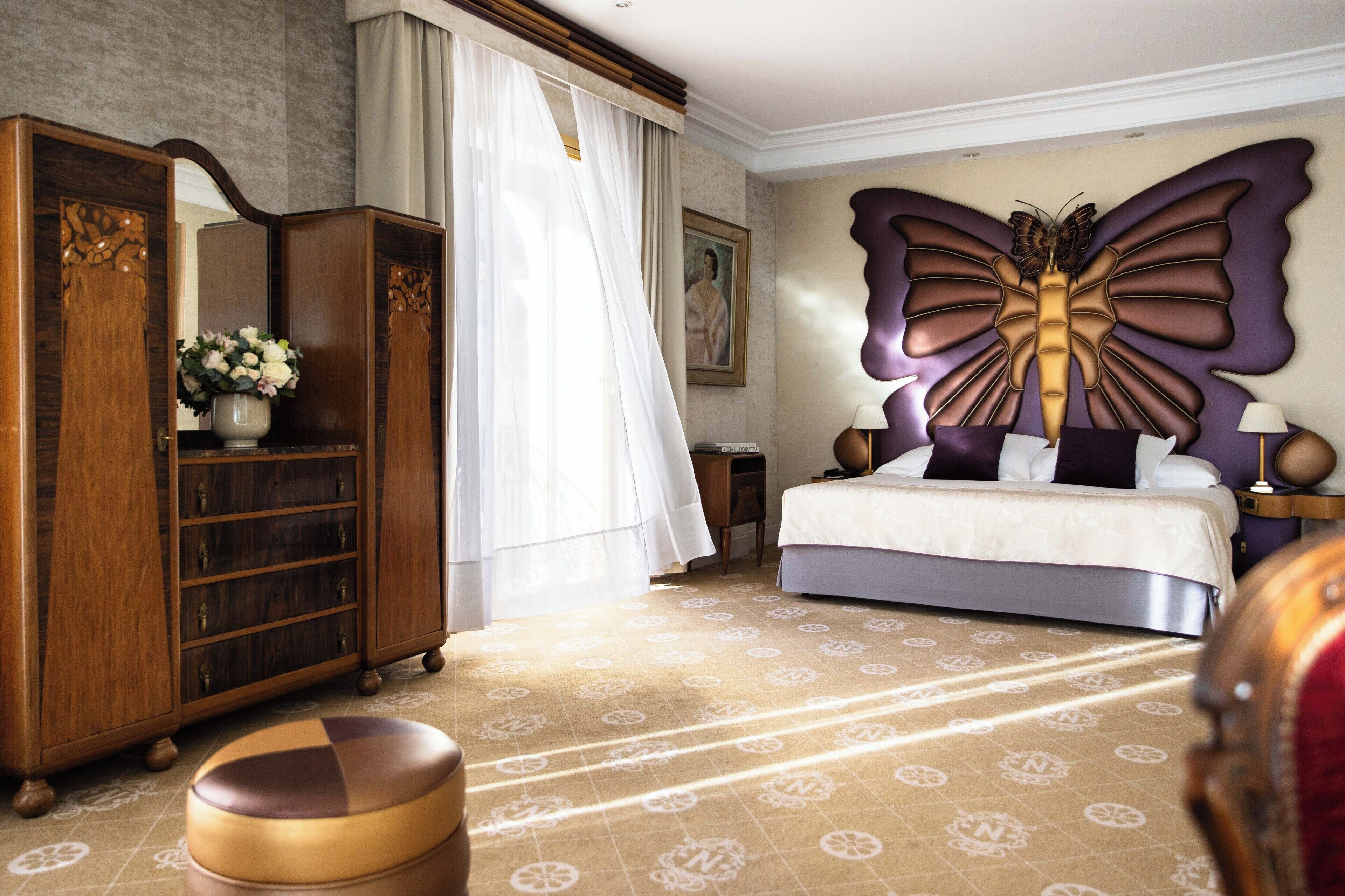 A bedroom with a large bed, a wardrobe, a mirror, and a decorative butterfly wall piece.