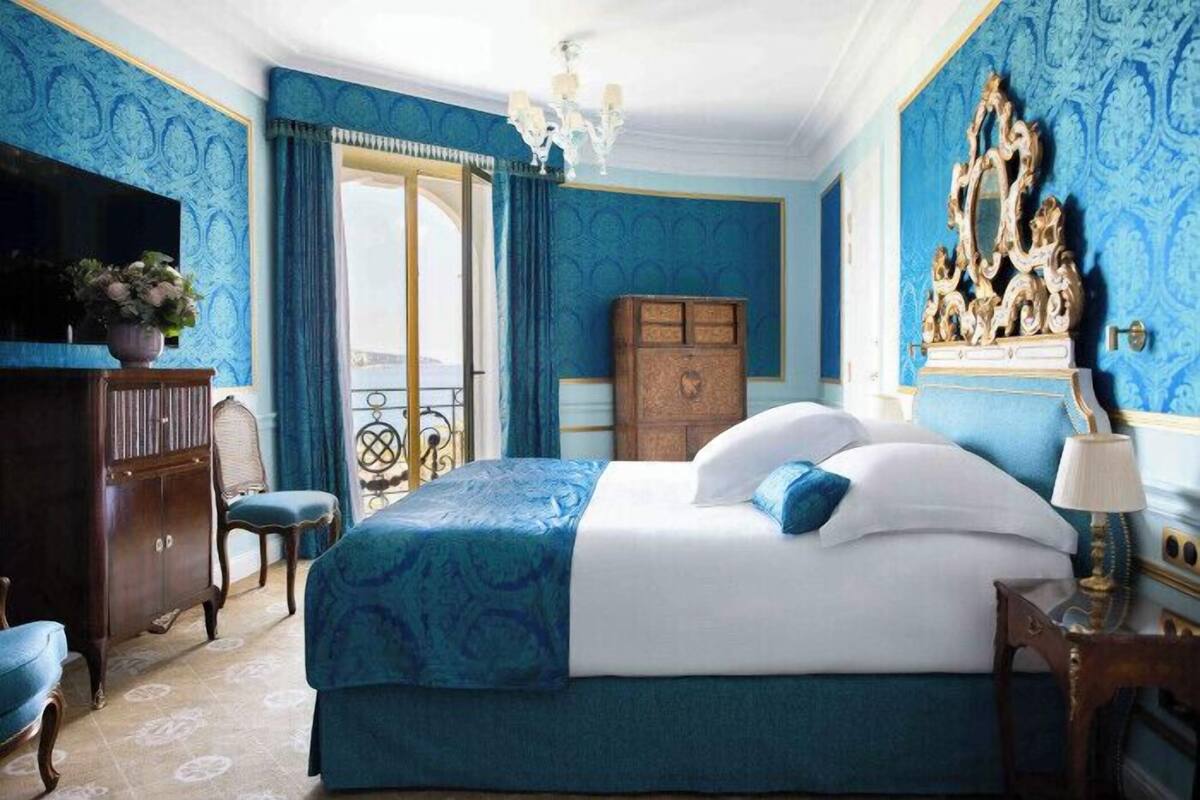 A bedroom with a large bed, a wooden wardrobe, a television, and a chandelier.
