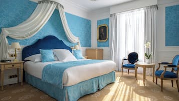 Un dormitorio con una cama grande, dosel, una silla, una mesa y un cuadro en la pared.